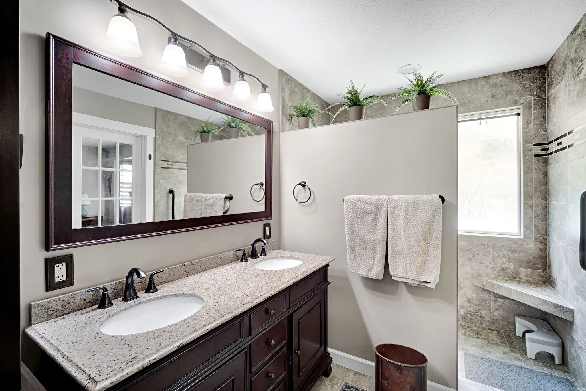 Updated primary bathroom featuring a dual sink vanity with granite countertop and dark wood-finish cabinetry.  Large walk in shower.