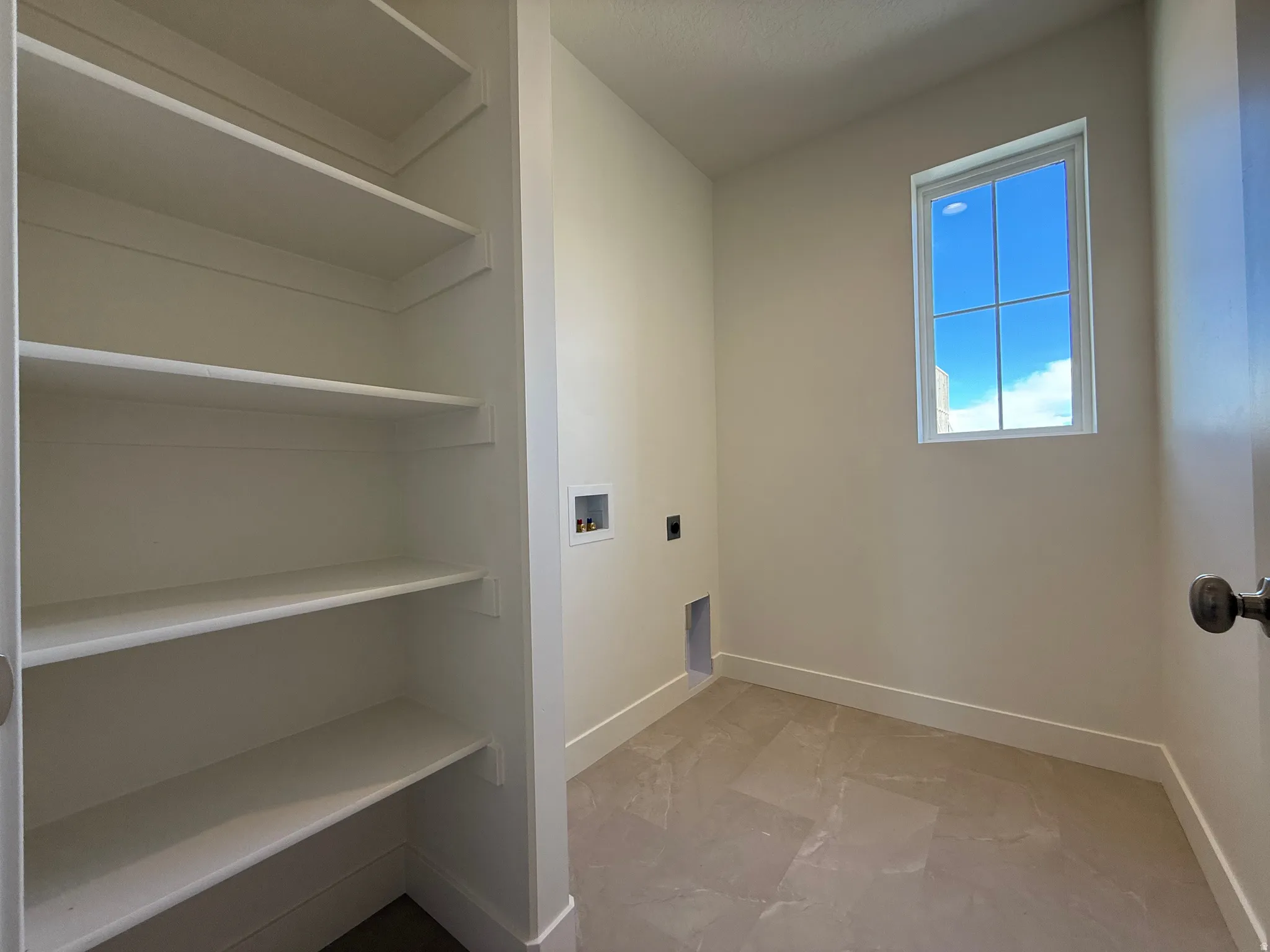 Dedicated laundry space featuring a window, built-in shelving, tiled flooring, and connections for appliances