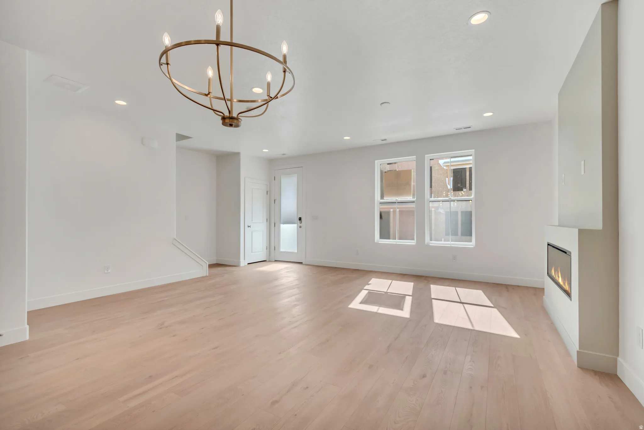 Spacious living area featuring light wood-finish flooring, a contemporary fireplace with a built-in electric insert, and multiple windows