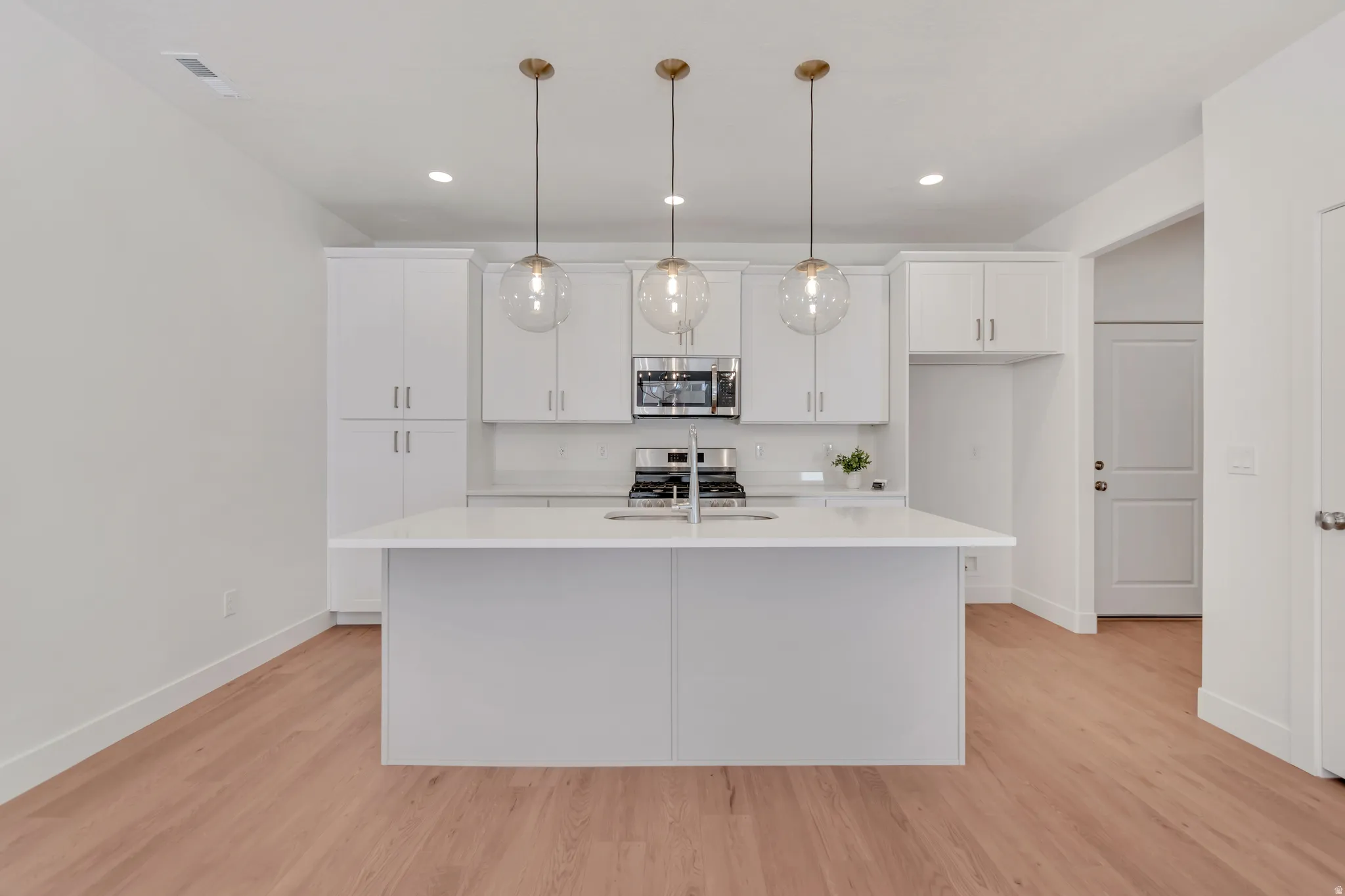 Kitchen featuring a central island with sink, white shaker cabinetry, stainless steel appliances, and light wood-finish flooring