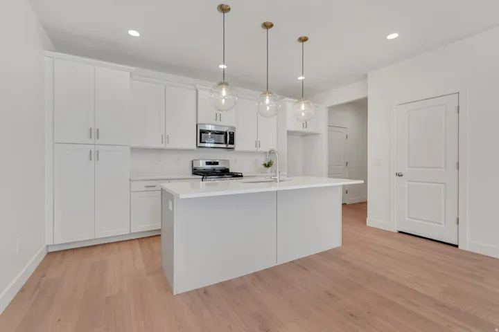 Contemporary kitchen featuring an expansive center island, white cabinetry, integrated stainless steel appliances, pendant lighting, and wood-finish flooring