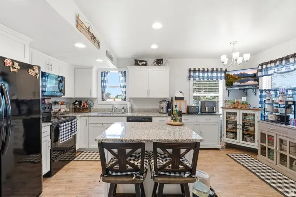 Kitchen featuring an island with stone-finish countertop, recessed lighting, wood-finish flooring, white cabinetry, and black appliances