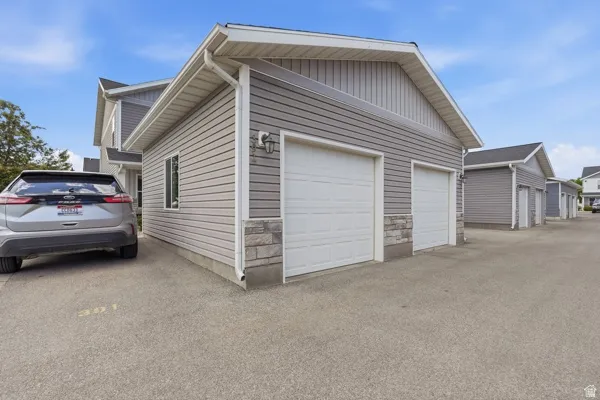 Two-car garage featuring white paneled doors, gray siding, and stone veneer accents