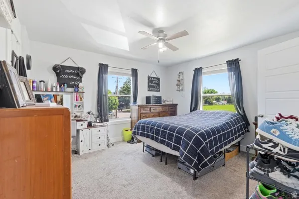 Carpeted bedroom featuring multiple windows, a ceiling fan with light fixture, and a paneled interior door
