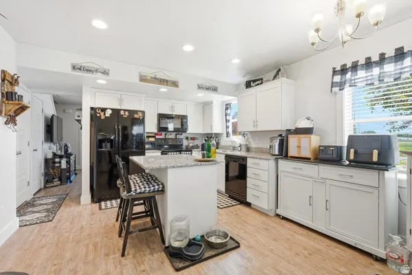 Kitchen featuring white cabinetry, black appliances, recessed lighting, wood-finish flooring, and a central island with a light-toned countertop