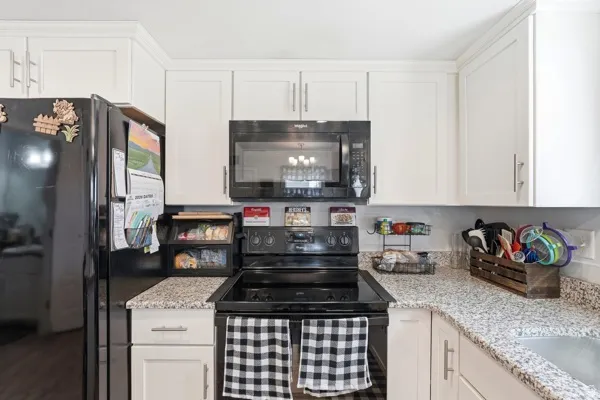 Kitchen featuring white cabinetry, speckled countertops, and black appliances