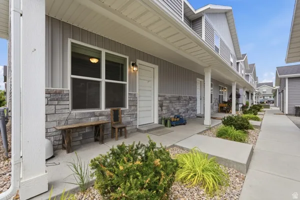 Exterior featuring gray vertical siding, stone veneer accents, white trim, a covered porch, and mature landscaping