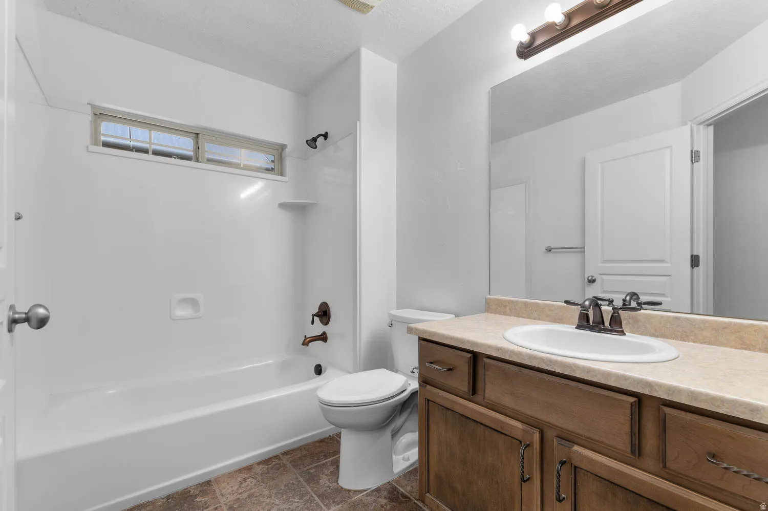 Bathroom featuring a white bathtub/shower combination with a transom window, a toilet, a vanity with a light-colored countertop, and a built-in mirror