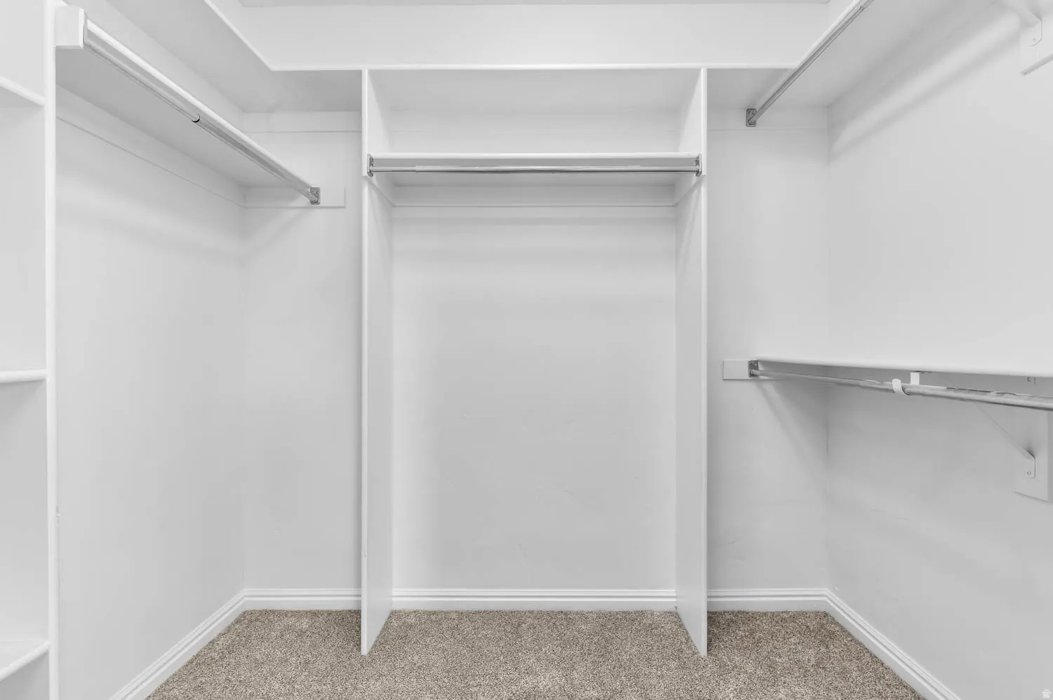 Walk-in closet with integrated white shelving, multiple chrome hanging rods, and neutral-toned carpet flooring
