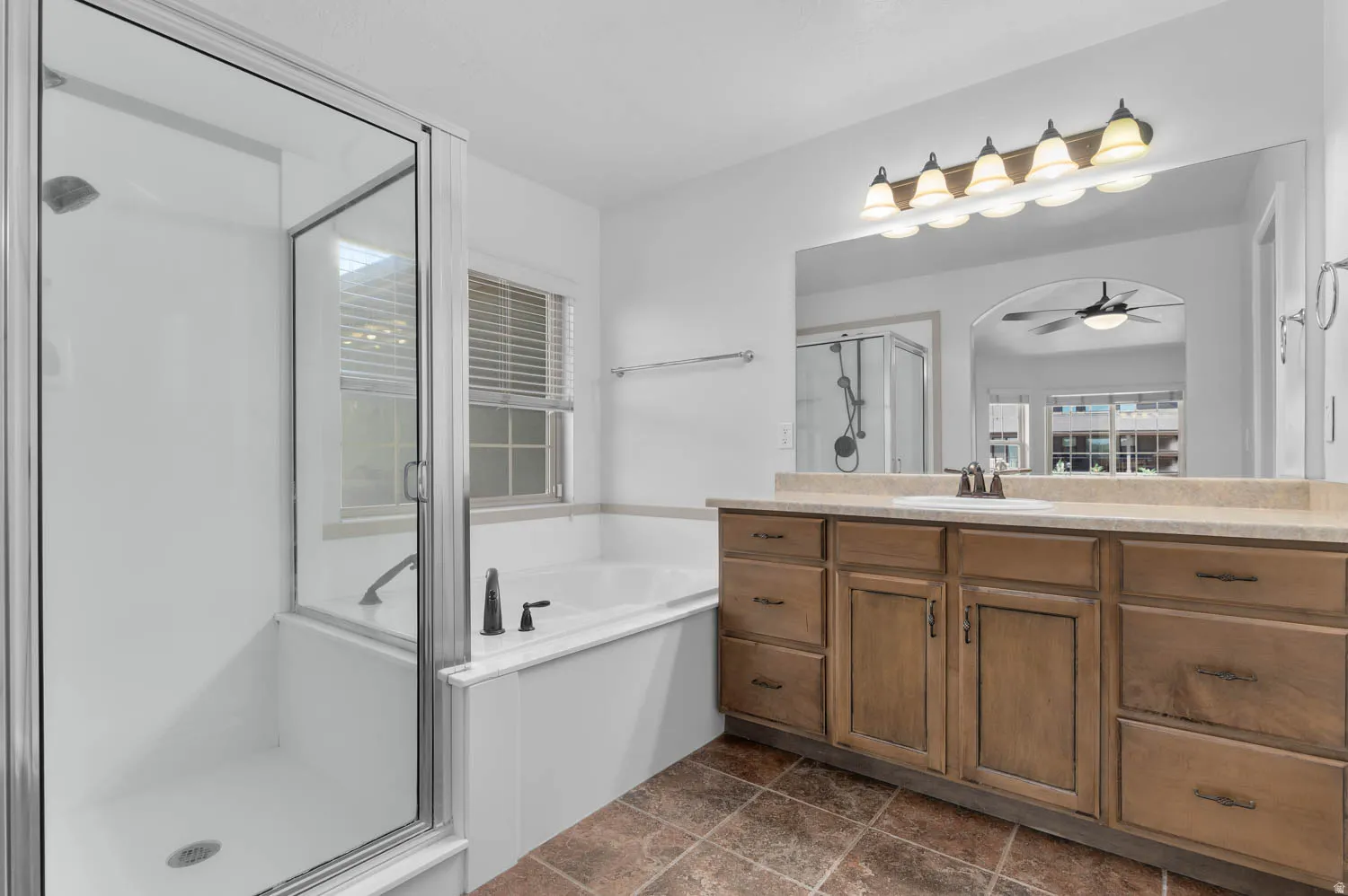 Bathroom featuring a glass-enclosed shower, a built-in tub with black fixtures, and a window with horizontal blinds