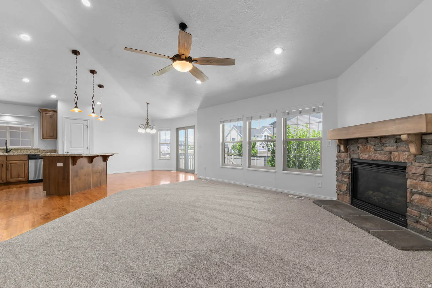 Open-concept living area featuring a stone-faced fireplace with a wood mantel, triple windows, and a ceiling fan