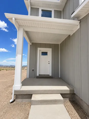 Covered entry porch featuring a solid white door with an upper window pane, flanked by vertical siding in a neutral tone