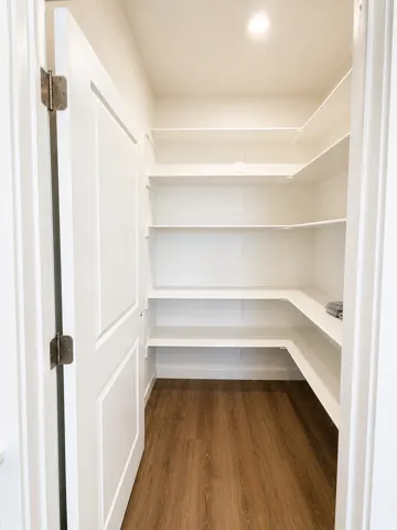 Walk-in pantry featuring extensive white shelving, wood-finish flooring, and recessed ceiling lighting