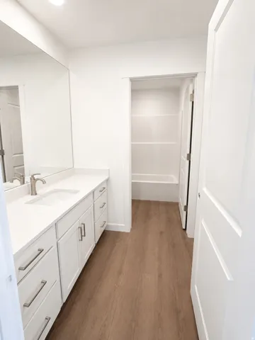Modern bathroom vanity featuring a white countertop, undermount sink, brushed nickel faucet, and wood-finish flooring