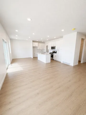 Open-concept living space featuring light wood-finish flooring, recessed ceiling lighting, and a kitchen with white cabinetry, stainless steel appliances, and a central island with a sink