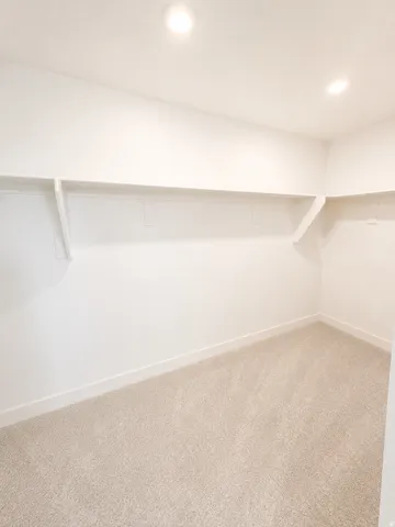 Carpeted closet space featuring integrated shelving, recessed lighting, and white baseboards