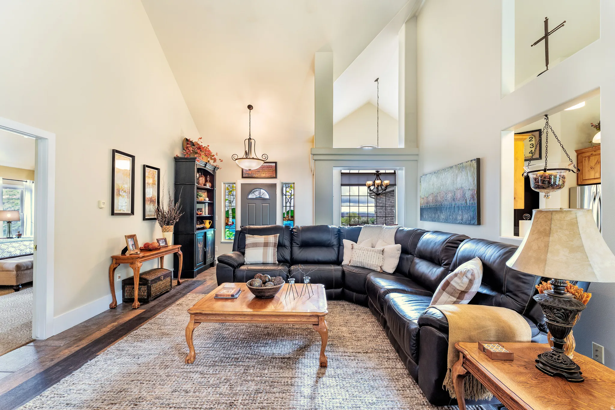 Spacious living area featuring vaulted ceilings, wood-finish flooring, and a large arched window with a chandelier