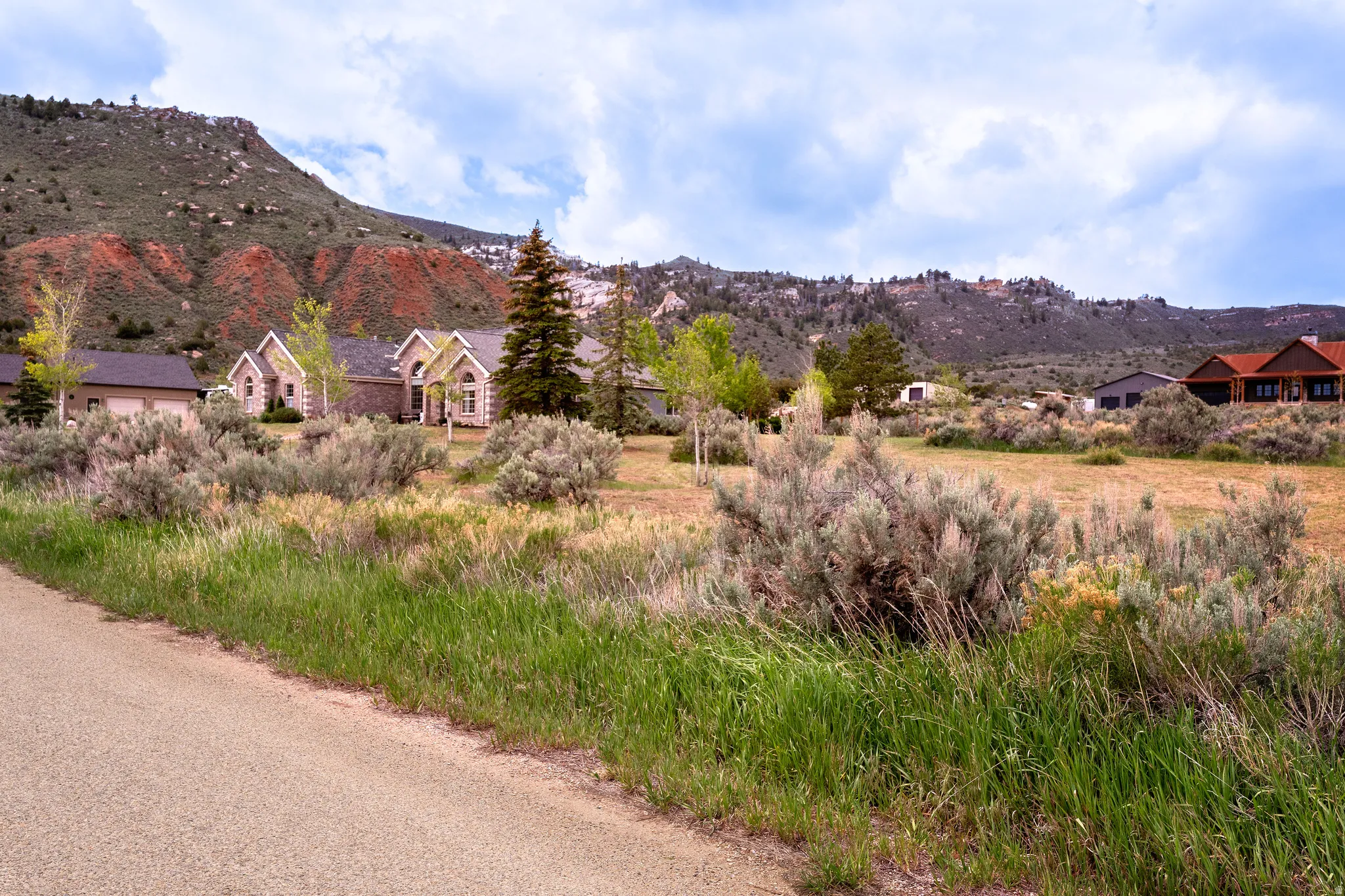 Scrubland terrain with natural vegetation and distant residential structures, all set against a backdrop of mountainous landscapes