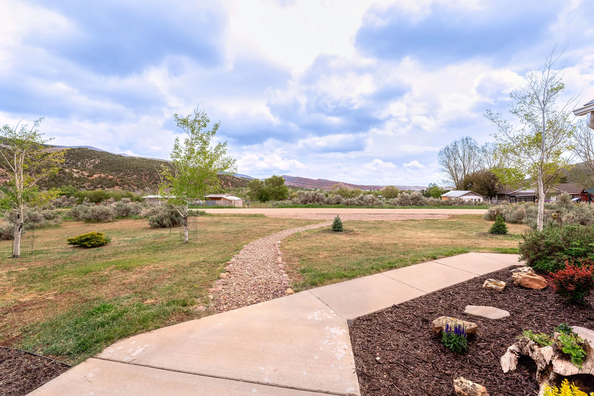 Manicured front yard with mature trees, a concrete pathway, and a decorative rock path
