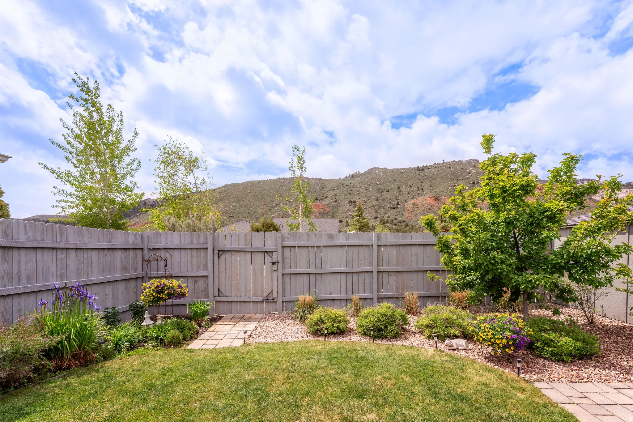 Fenced backyard featuring a manicured lawn, established landscaping, a stepping stone pathway, and a mountain backdrop
