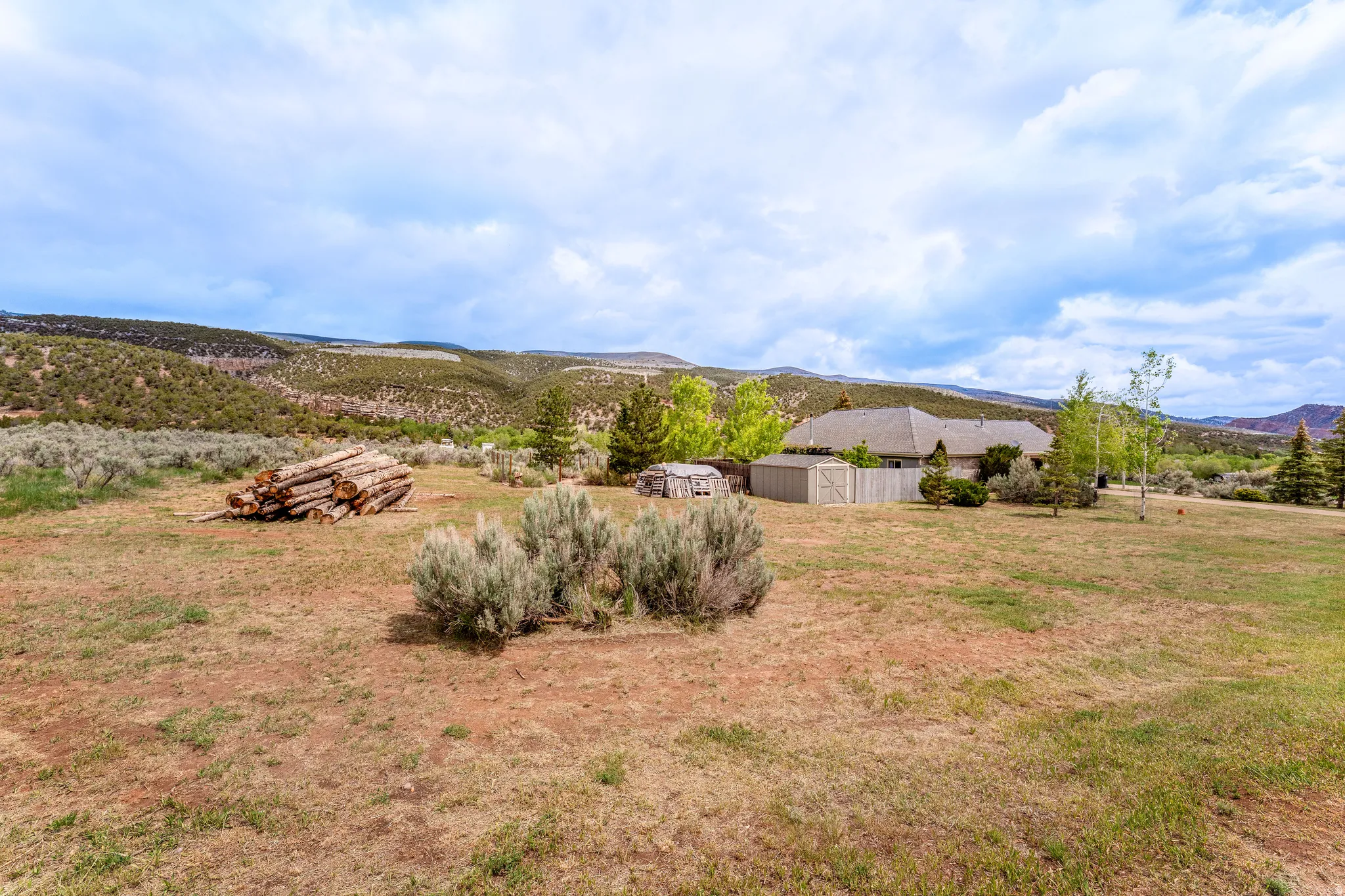 Expansive property featuring a single-story residence with a composite shingle roof, a privacy fence, and multiple exterior sheds