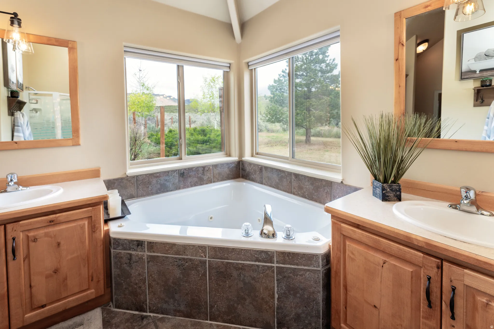 Corner jetted tub set within tiled surround, featuring two large windows overlooking a natural landscape