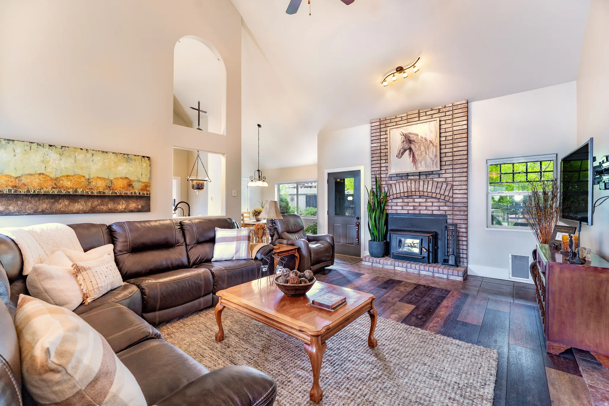 Spacious living area featuring vaulted ceilings, a brick fireplace with a wood-burning insert, LVP flooring, and a ceiling fan