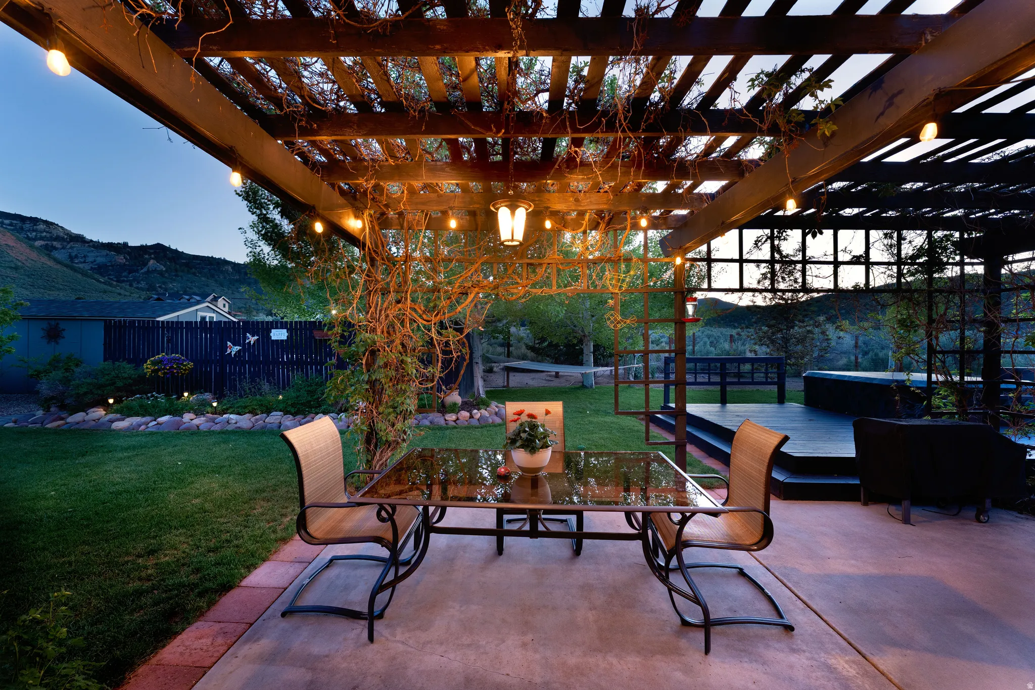 Expansive outdoor living area featuring a wooden pergola with string lights, a concrete patio, and a separate elevated deck