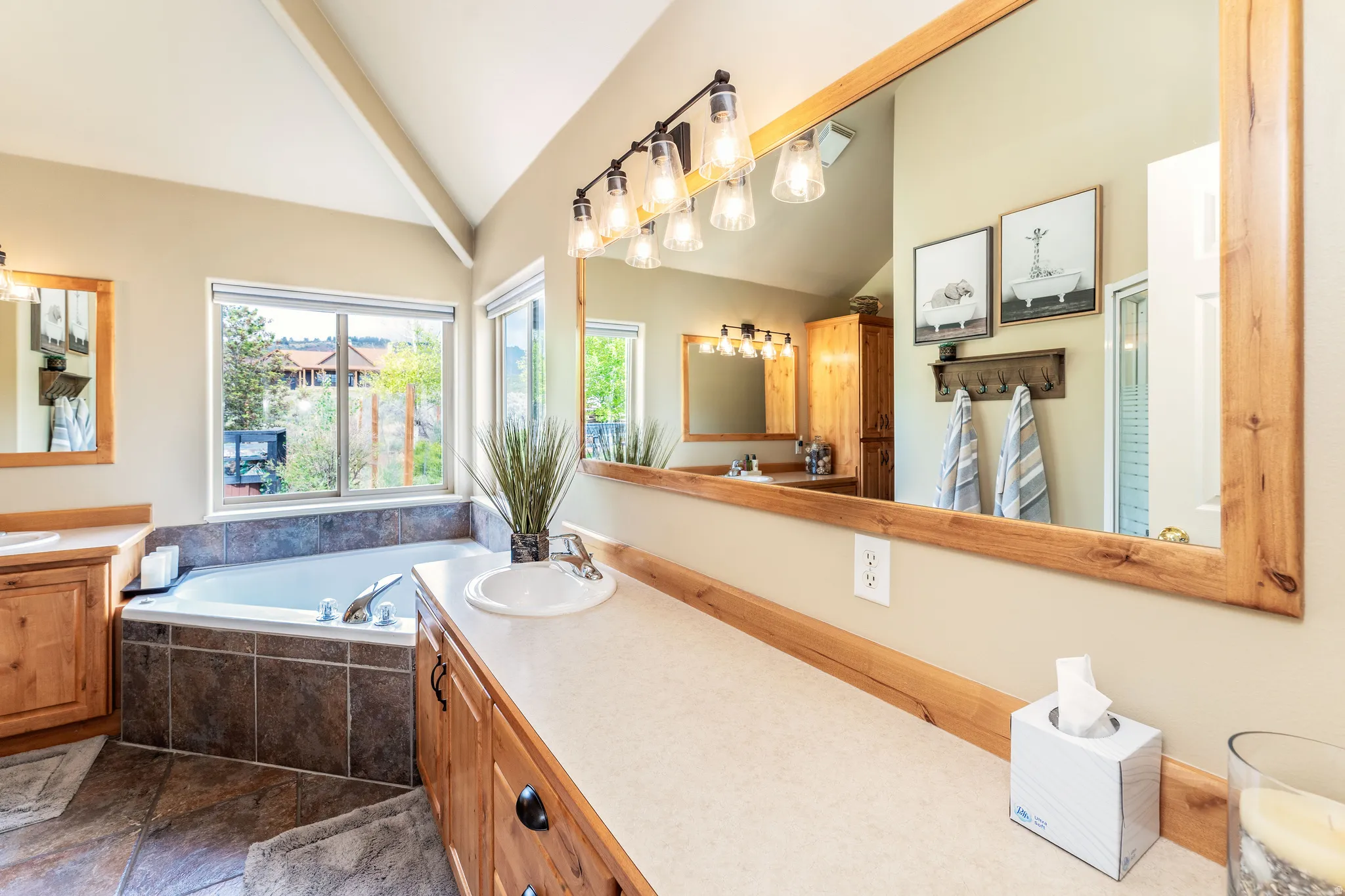 Master Bathroom featuring a soaking tub with tile surround, dual wood-finish vanities, large mirrors and vaulted ceilings