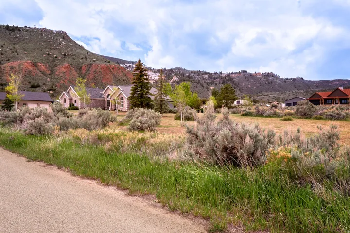 Scrubland terrain with natural vegetation and distant residential structures, all set against a backdrop of mountainous landscapes
