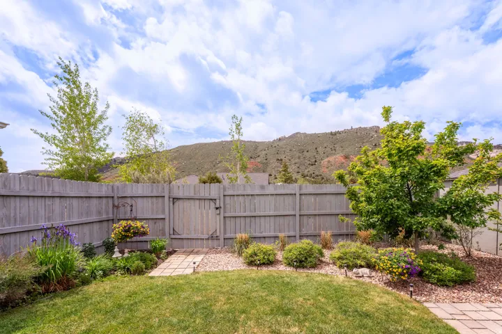 Fenced backyard featuring a manicured lawn, established landscaping, a stepping stone pathway, and a mountain backdrop