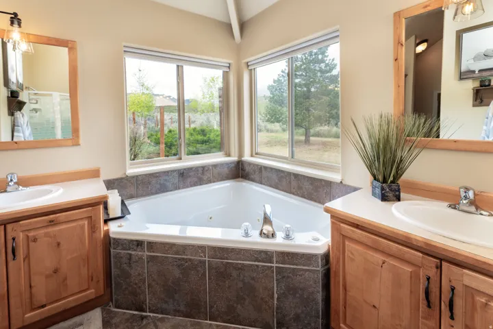 Corner jetted tub set within tiled surround, featuring two large windows overlooking a natural landscape
