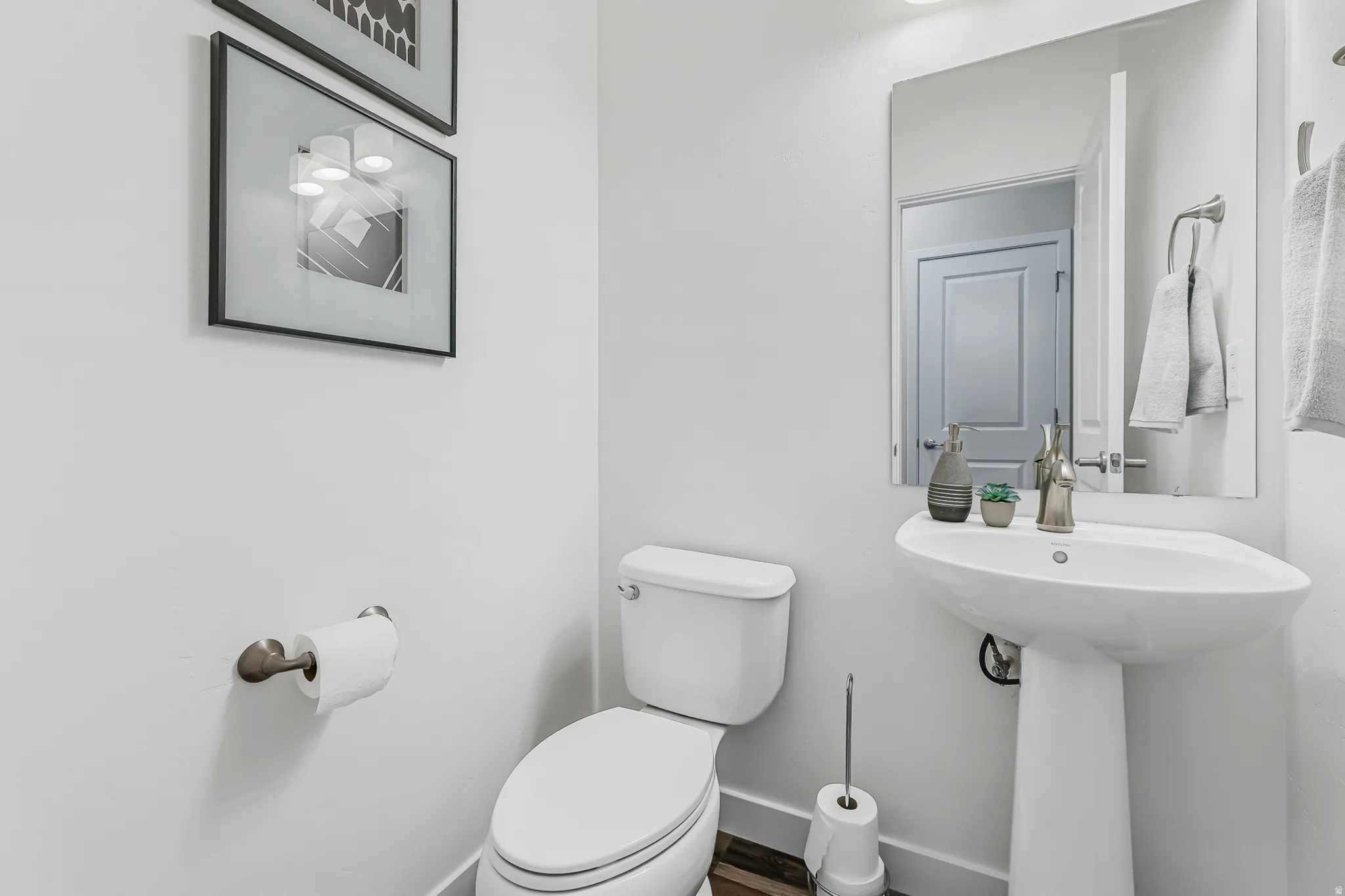 Modern powder room featuring a white pedestal sink, coordinating toilet, brushed nickel faucet