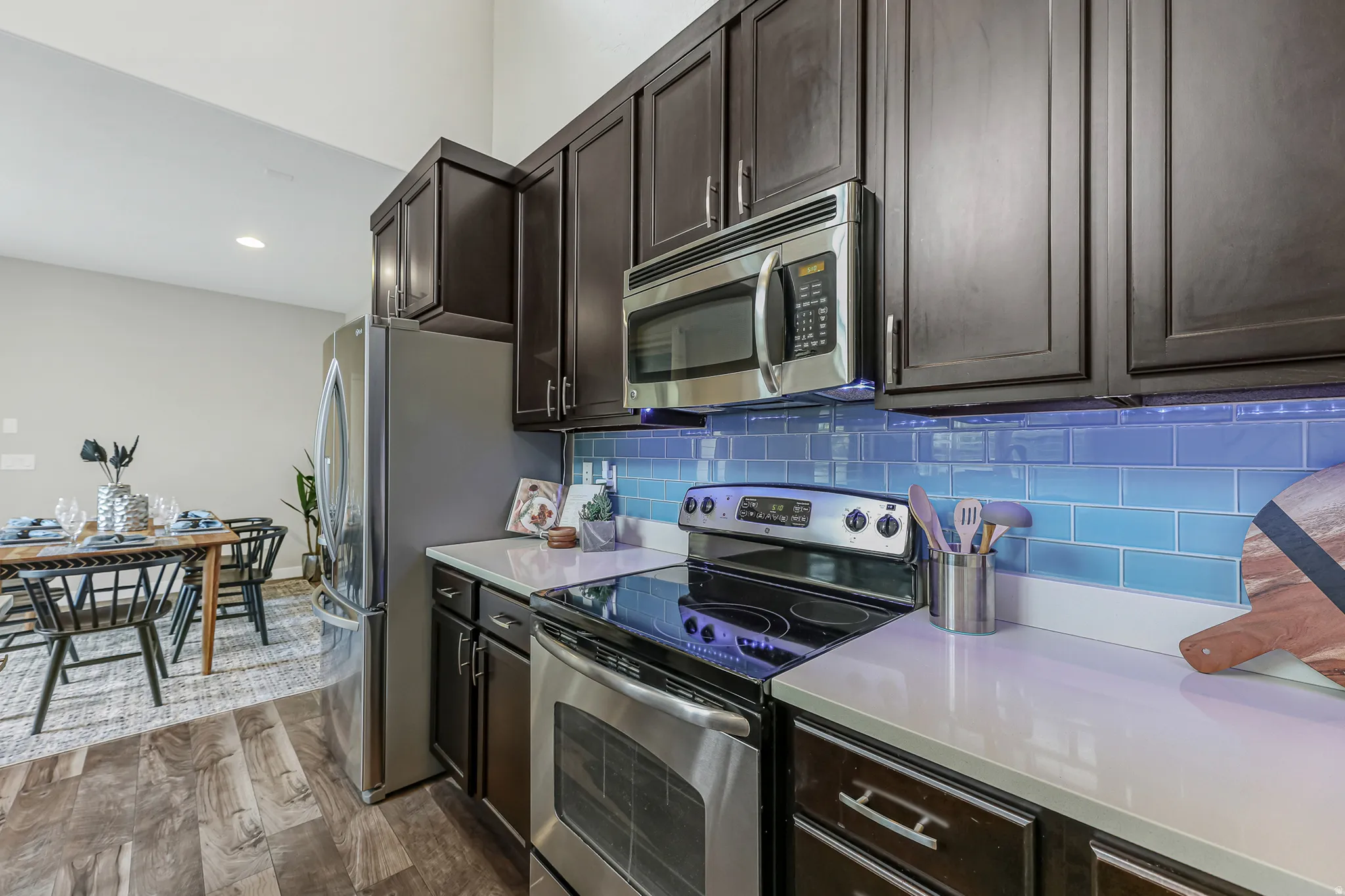 Kitchen featuring dark wood cabinetry, stainless steel appliances, light countertops, and a blue subway tile backsplash