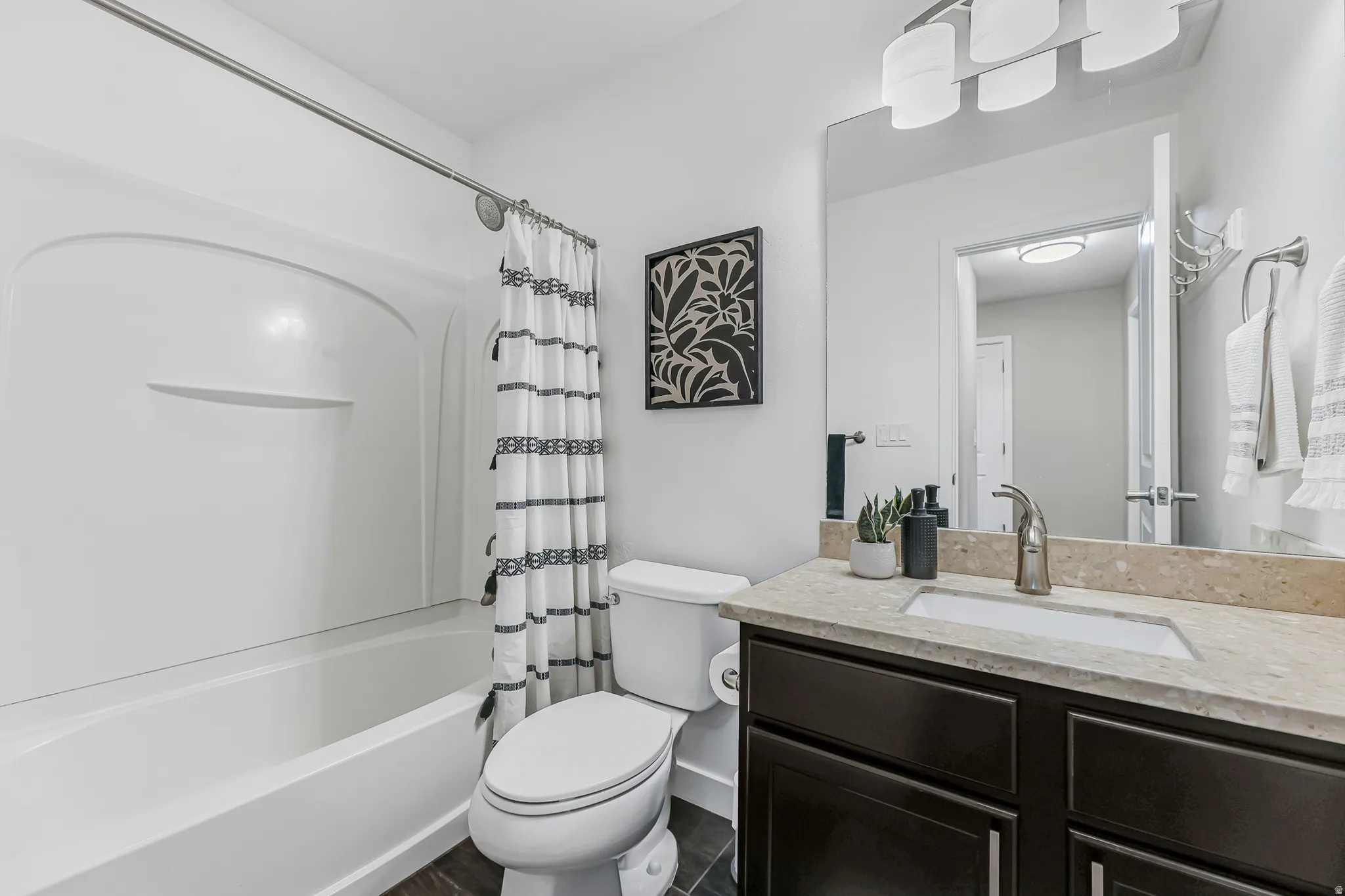 Bathroom featuring a white tub/shower combination, dark wood-finish vanity with a light-toned countertop, and a rectangular undermount sink with a single-handle faucet