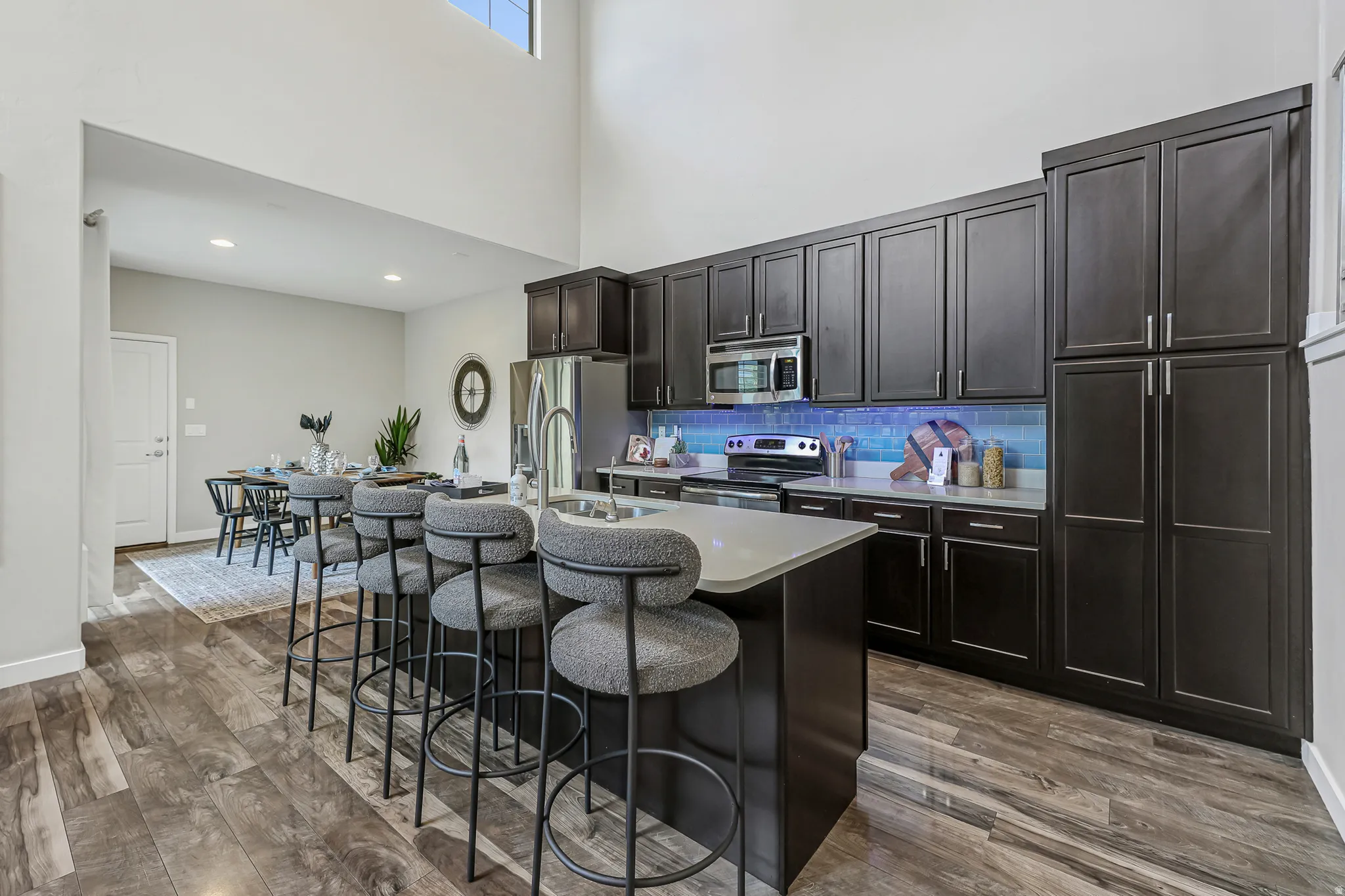 Spacious kitchen featuring dark wood cabinetry, stainless steel appliances, a large island with an integrated sink, light-toned countertops, and wood-finish flooring