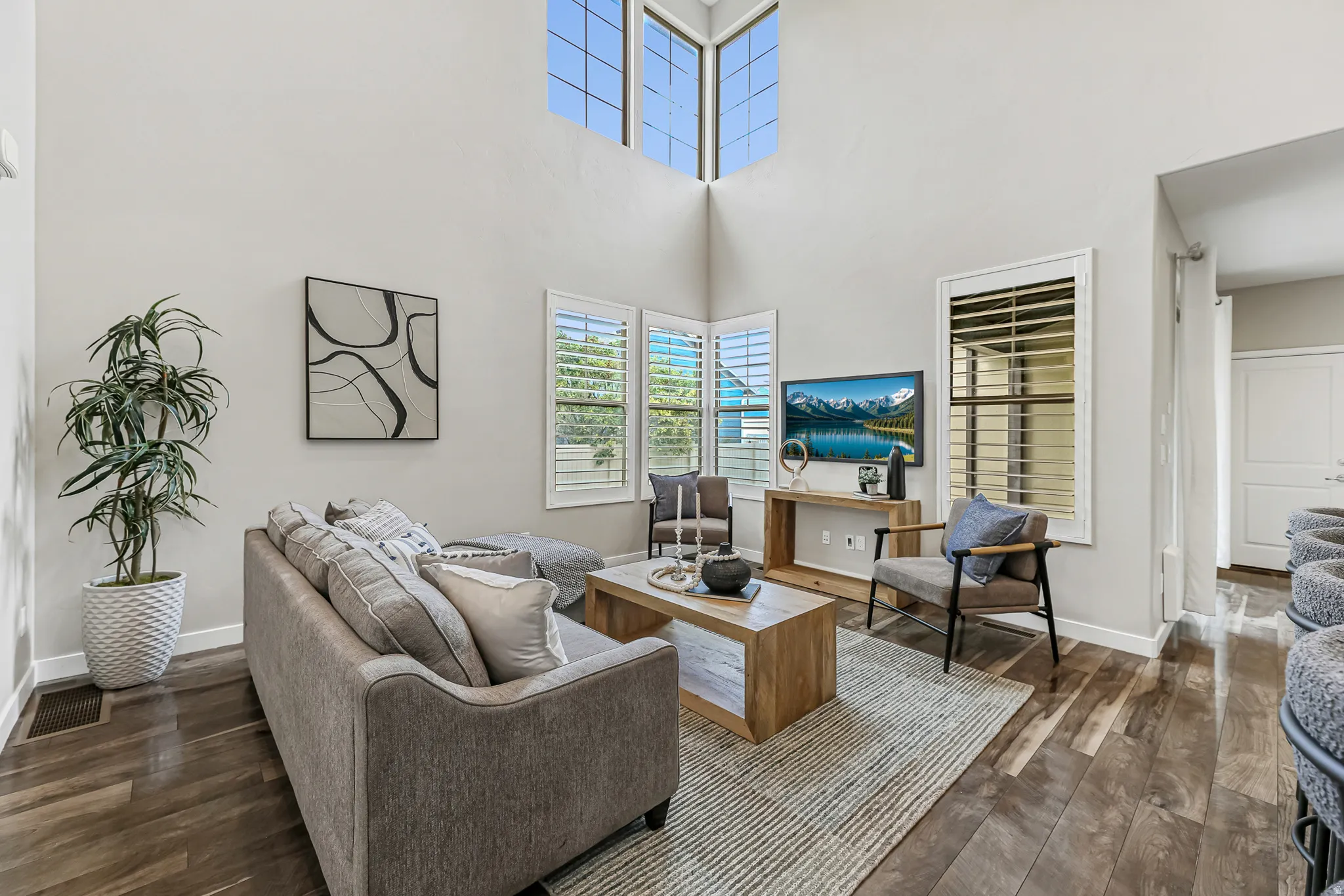 High ceiling living area featuring wood-finish flooring, plantation shutters, and tall windows
