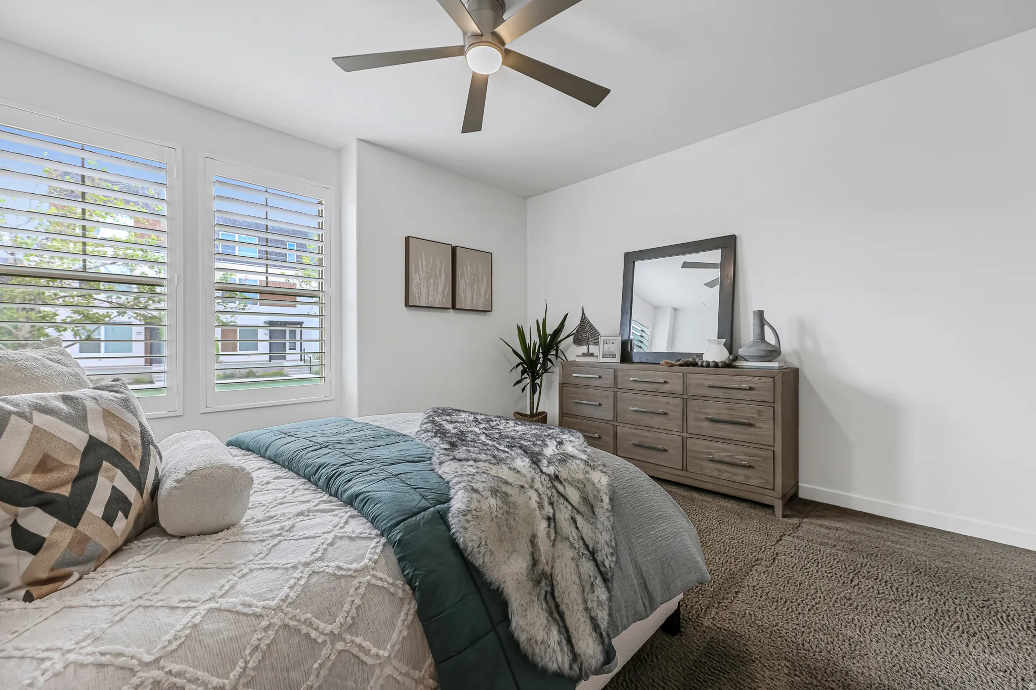Spacious primary bedroom featuring multiple windows with plantation shutters, ceiling fan with integrated lighting, and neutral wall tones