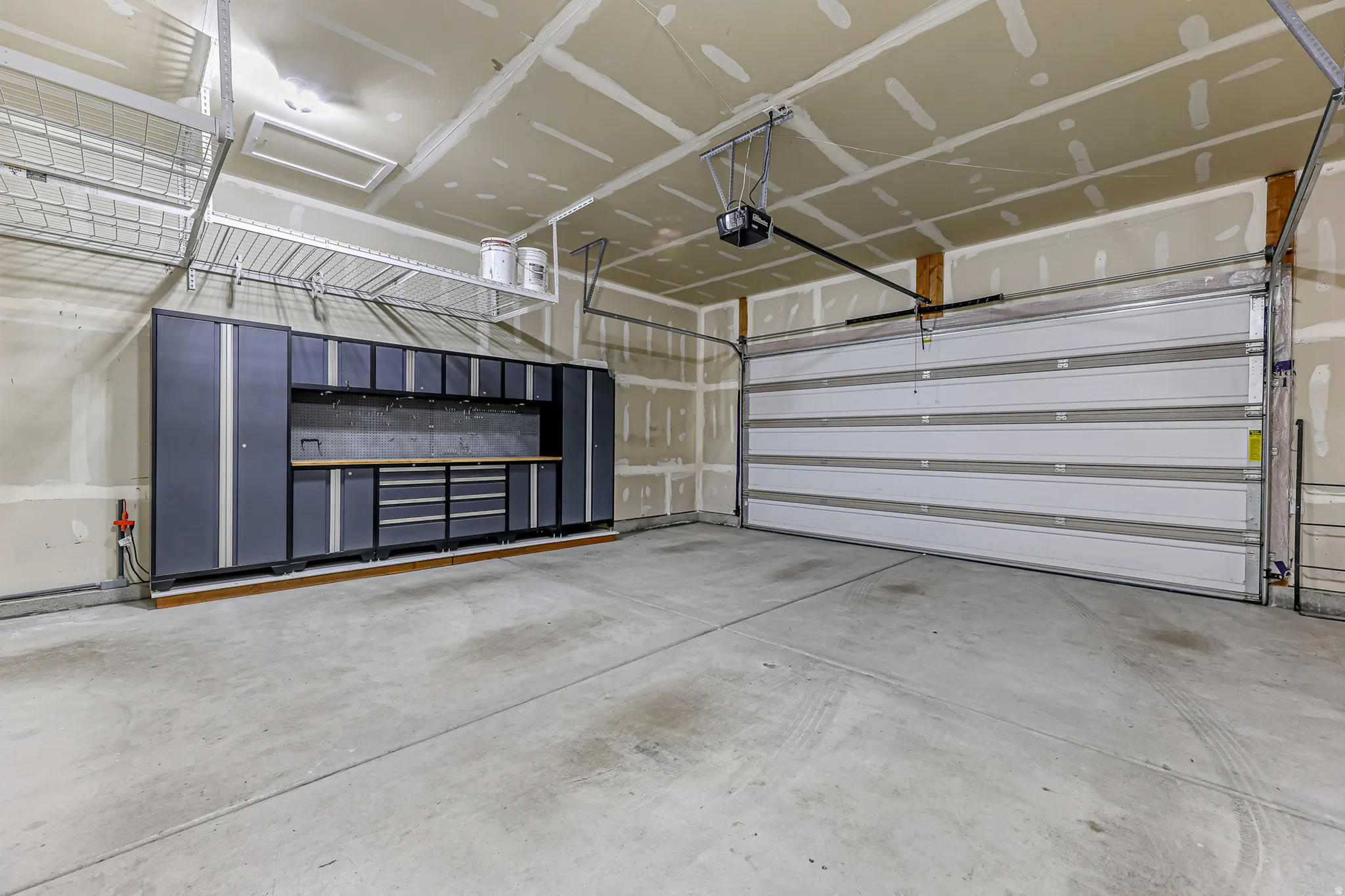 Spacious garage featuring a large white sectional door, extensive built-in cabinetry with a wood-finish countertop, overhead wire shelving, and a concrete floor