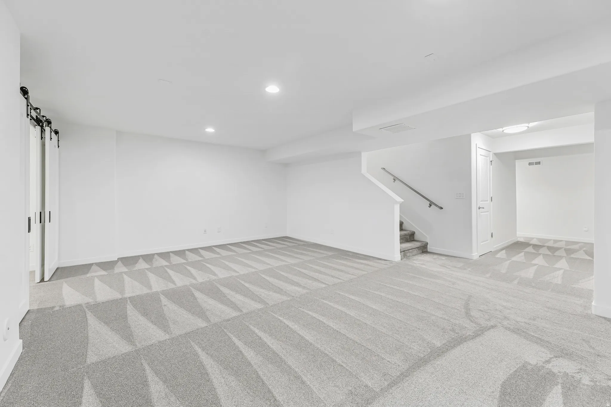 Spacious basement family room featuring patterned carpet, recessed lighting, white walls, and barn doors