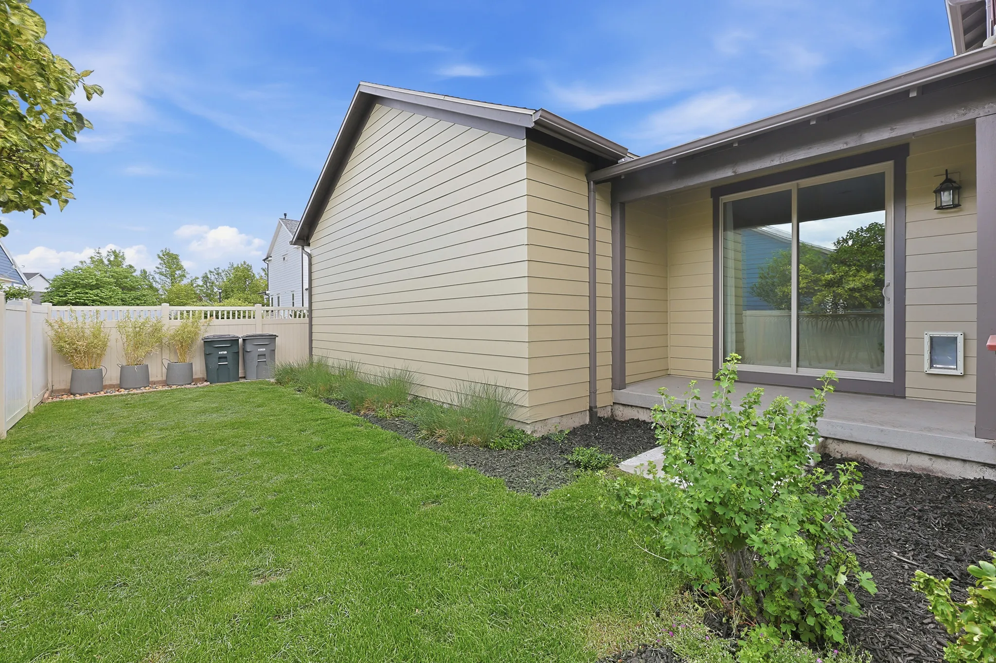 Private backyard featuring a manicured lawn, white privacy fence, and a concrete patio