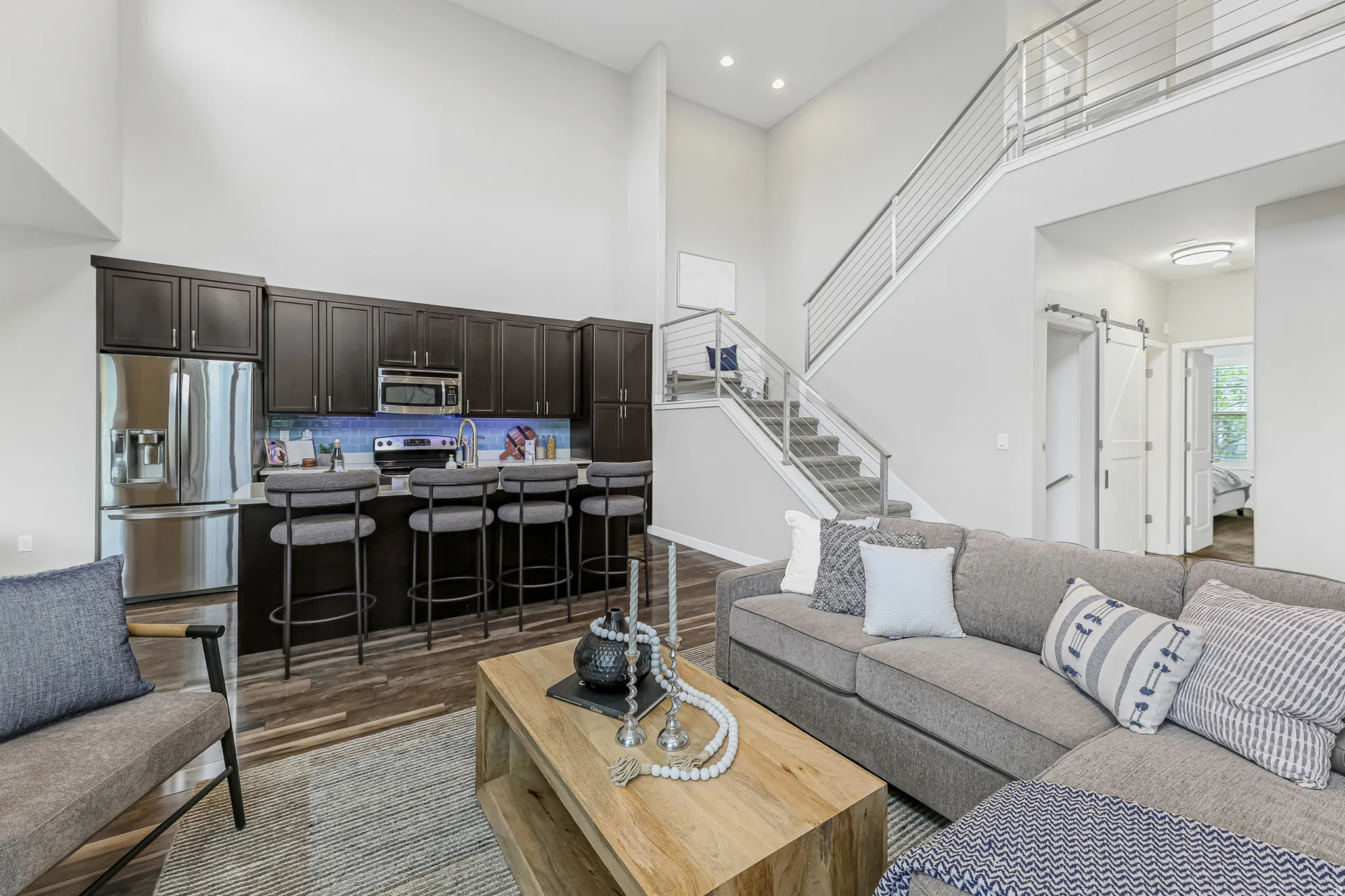 Open-concept living area featuring high ceilings, dark wood-finish flooring, a contemporary kitchen island with seating, and modern staircase with cable railing