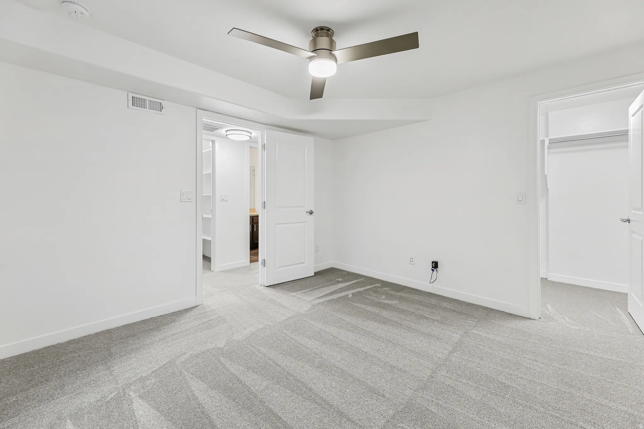 Spacious basement bedroom featuring light gray patterned carpeting, a contemporary ceiling fan with integrated lighting, and white baseboards