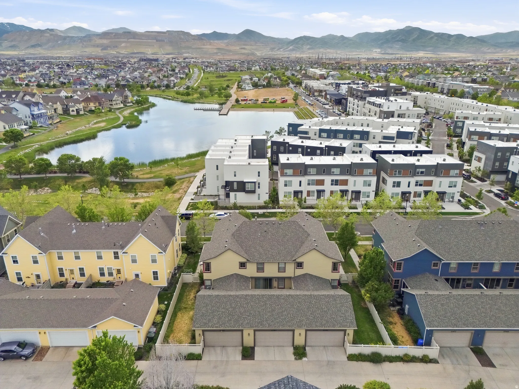Aerial perspective showcasing a community with varied architectural styles, a prominent lake, extensive green spaces, and mountain backdrops