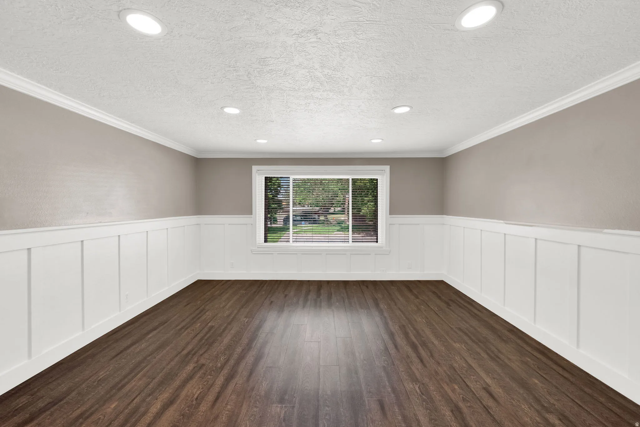 Spacious room featuring rich wood-finish flooring, crisp white wainscoting, and crown molding