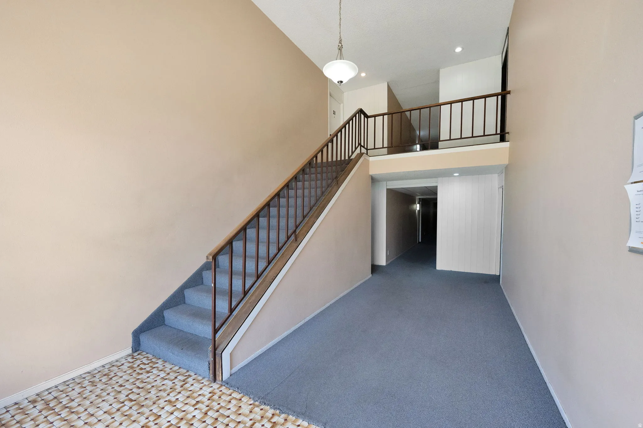 Two-story entryway featuring a carpeted staircase with wood and metal railings, light beige painted walls, and an overhead pendant light fixture