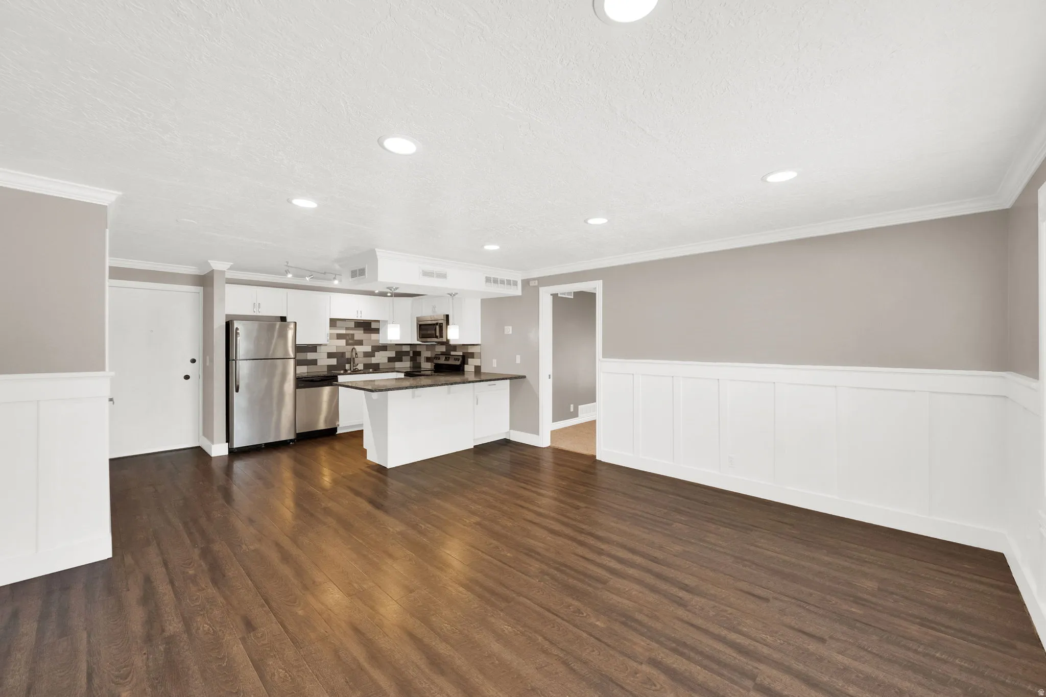 Open-concept living area featuring wood-finish flooring, recessed lighting, and wainscoting