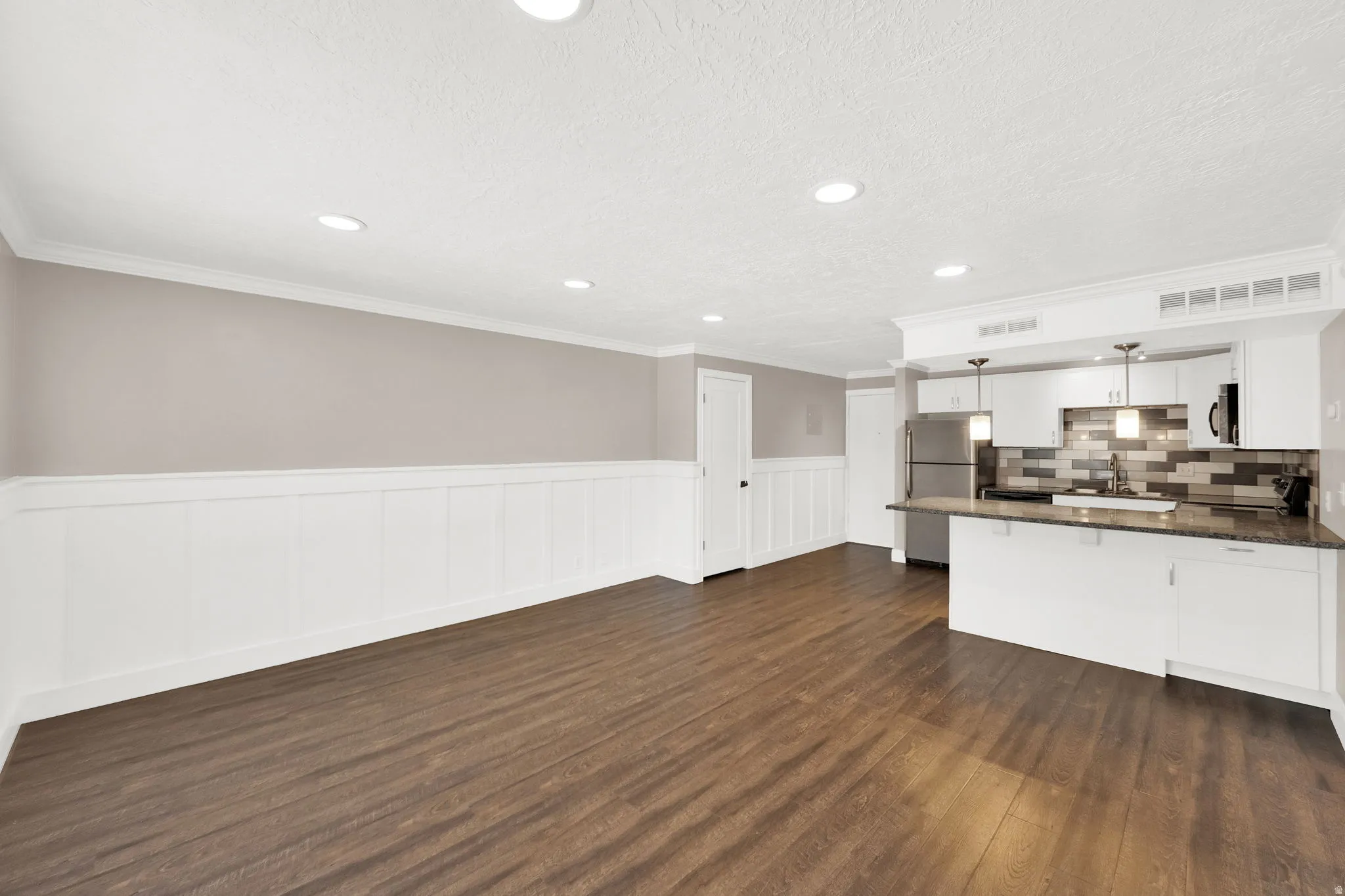 Expansive open-concept living area featuring wood-finish flooring, wainscoting, and recessed lighting