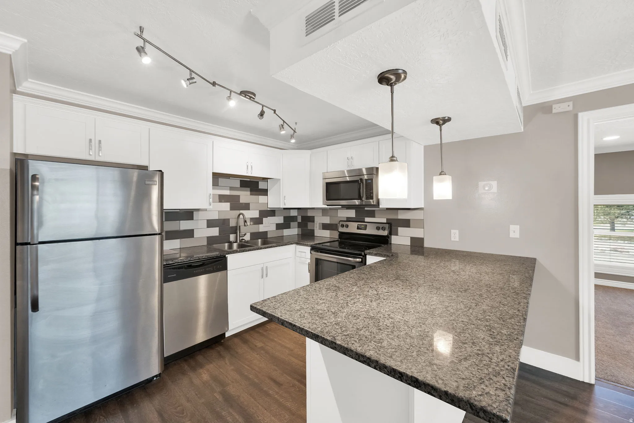 Kitchen featuring white cabinetry, stainless steel appliances, a grey and white tile backsplash, wood-finish flooring, and a stone countertop with a breakfast bar