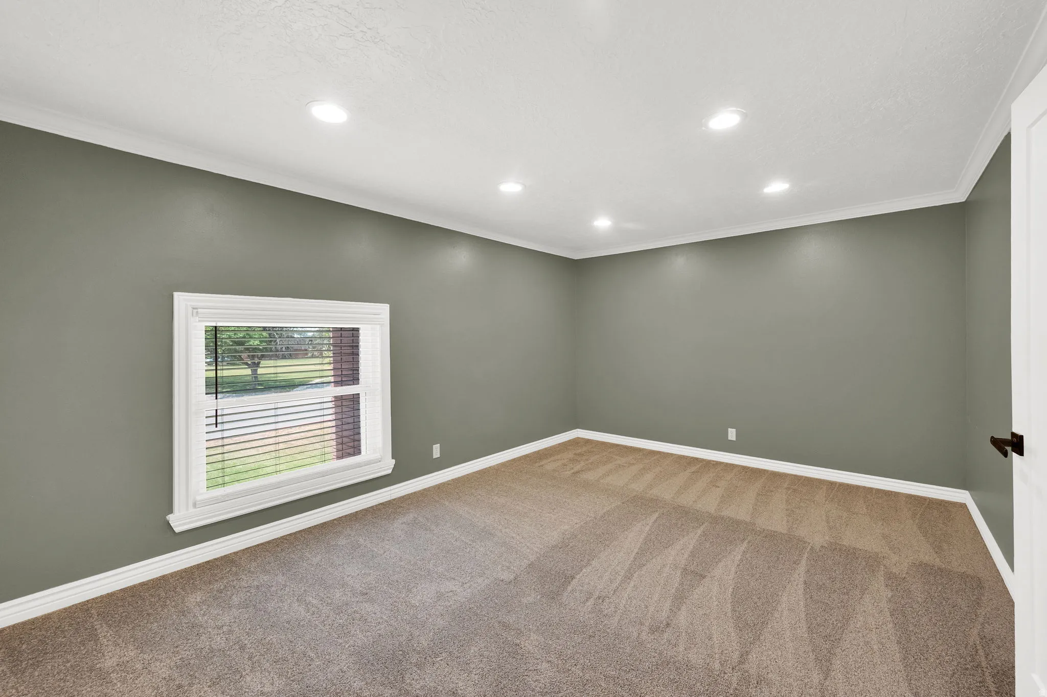 Room featuring neutral carpet flooring, recessed ceiling lighting, a white trim window with blinds, and contrasting wall color
